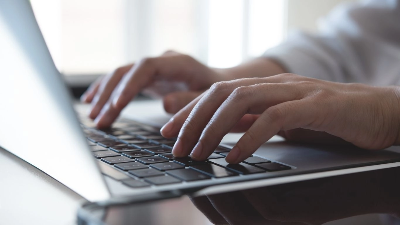 Mains tapant sur le clavier d’un ordinateur portable, illustrant la rédaction, la configuration ou la gestion de campagnes digitales.