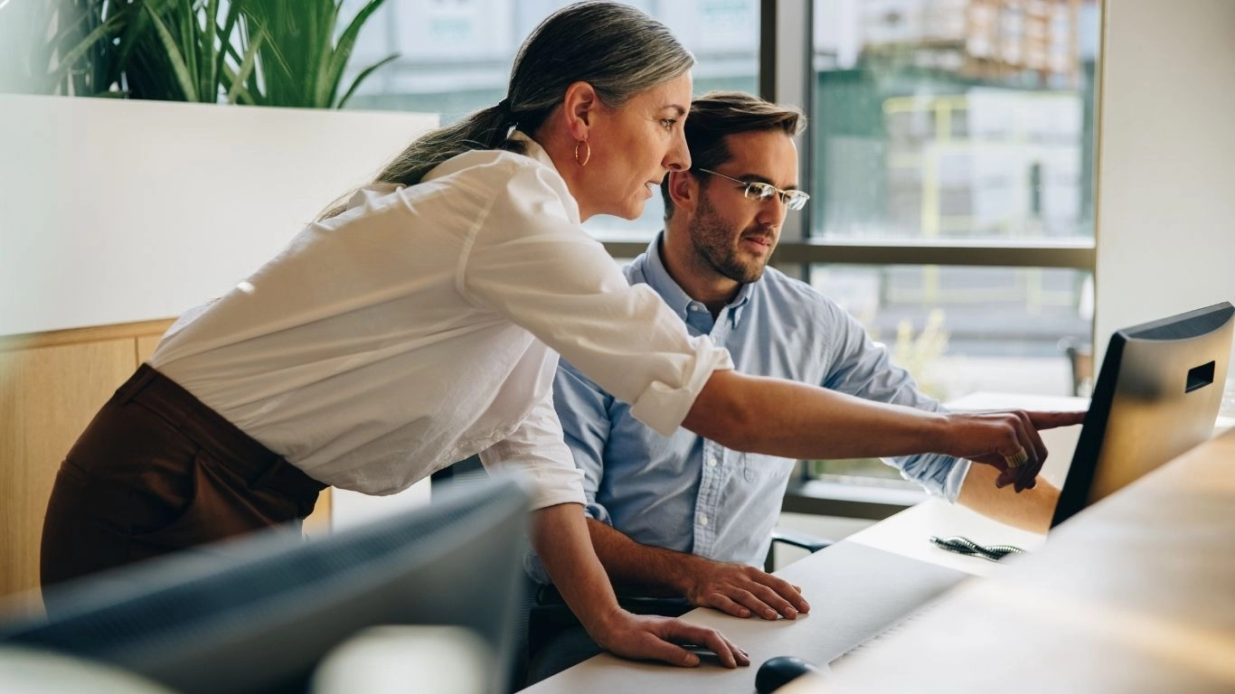 Formatrice accompagnant un participant devant un ordinateur, illustrant une formation HTML email de niveau débutant.
