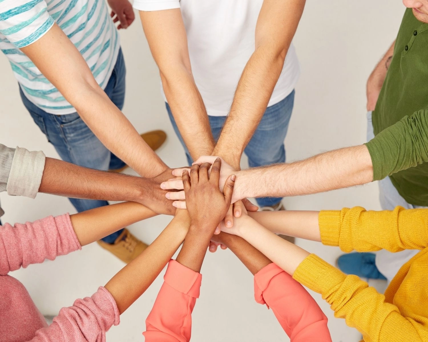 Groupe de personnes joignant leurs mains au centre, illustrant la collaboration, l’esprit d’équipe et l’engagement collectif.